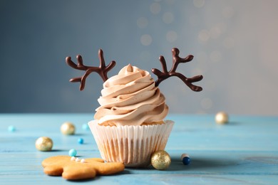Photo of Tasty Christmas cupcake with chocolate reindeer antlers, gingerbread man and festive decor on light blue wooden table