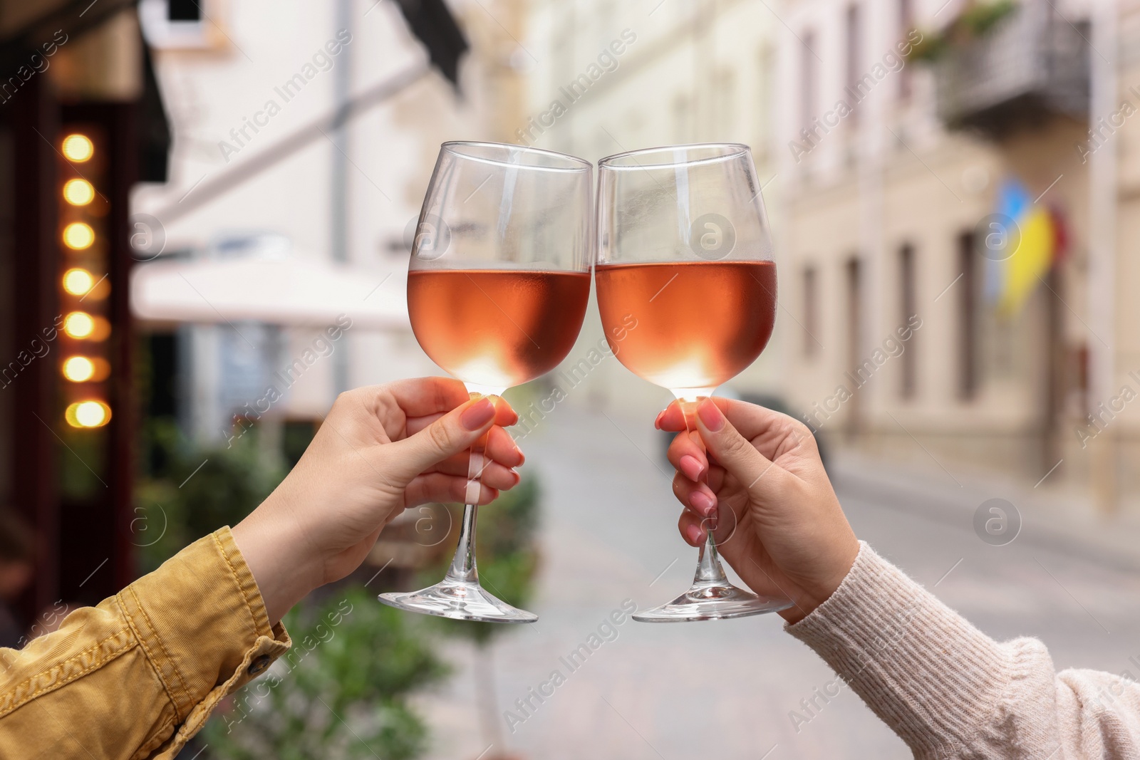 Photo of Women clinking glasses with rose wine outdoors, closeup