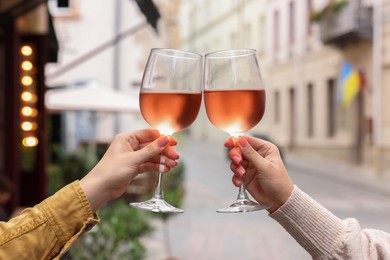 Photo of Women clinking glasses with rose wine outdoors, closeup