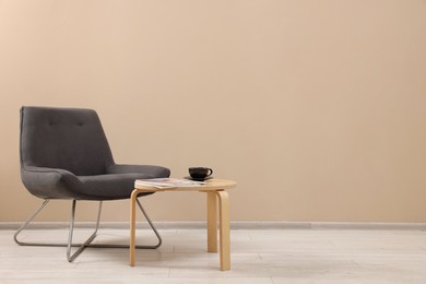 Photo of Comfortable armchair and coffee table near beige wall indoors, space for text. Interior design