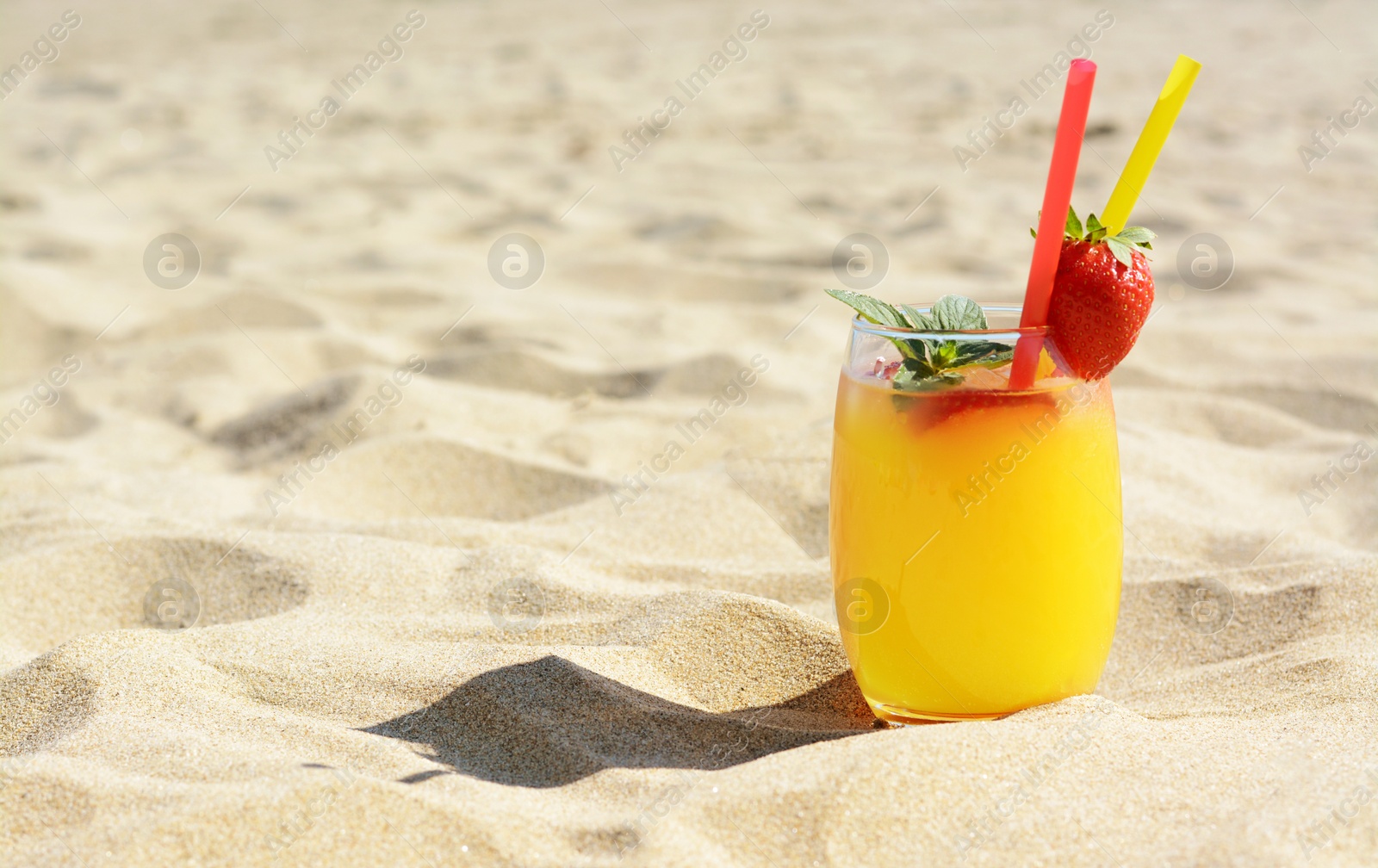 Photo of Glass of refreshing drink with strawberry on sandy beach, space for text