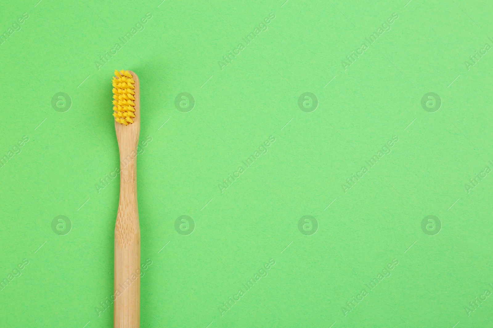 Photo of Natural bamboo toothbrush on green background, top view. Space for text