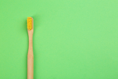 Photo of Natural bamboo toothbrush on green background, top view. Space for text