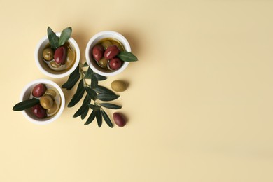 Photo of Bowls with different ripe olives and leaves on beige background, flat lay. Space for text