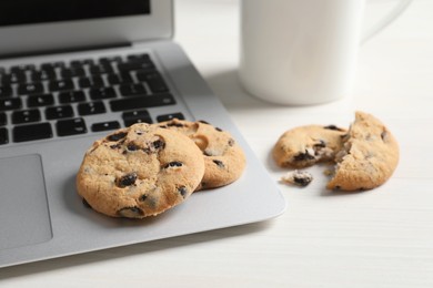 Chocolate chip cookies and laptop on white wooden table, closeup. Space for text