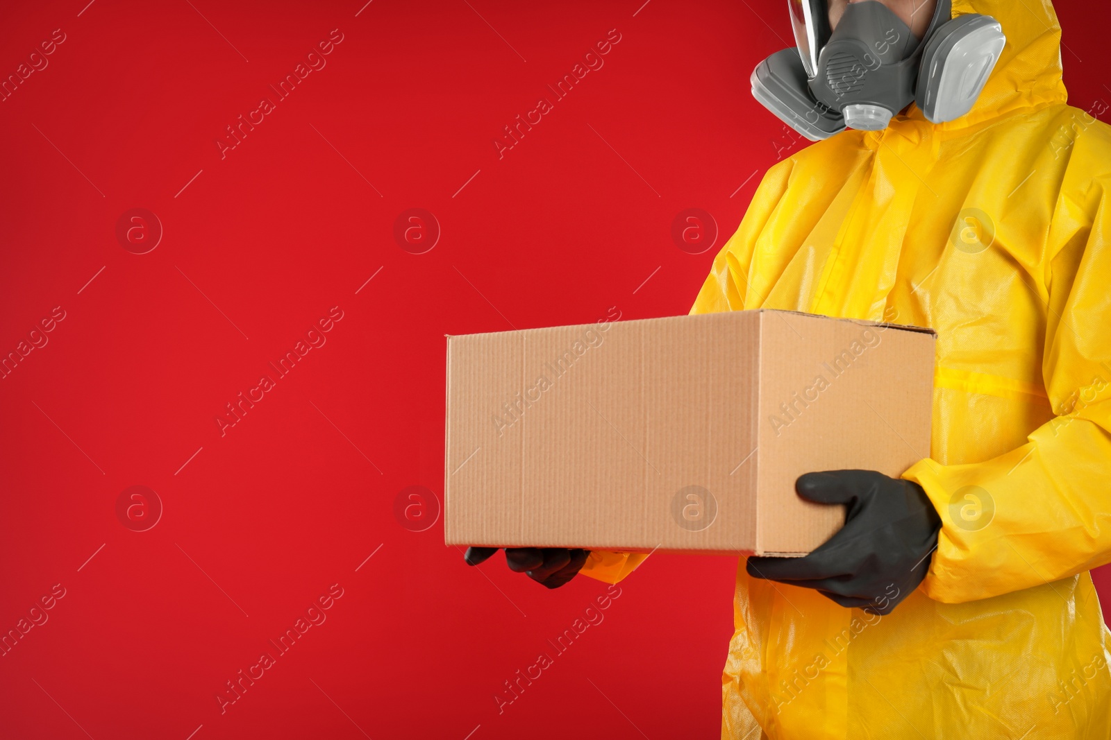 Photo of Man in chemical protective suit holding cardboard box on red background, closeup view with space for text. Prevention of virus spread