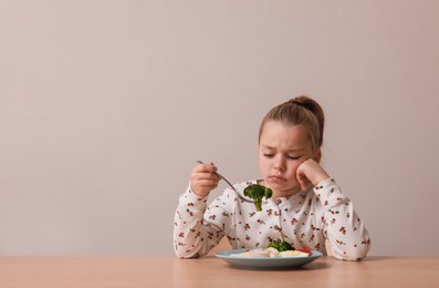 Cute little girl refusing to eat her dinner at table on grey background, space for text