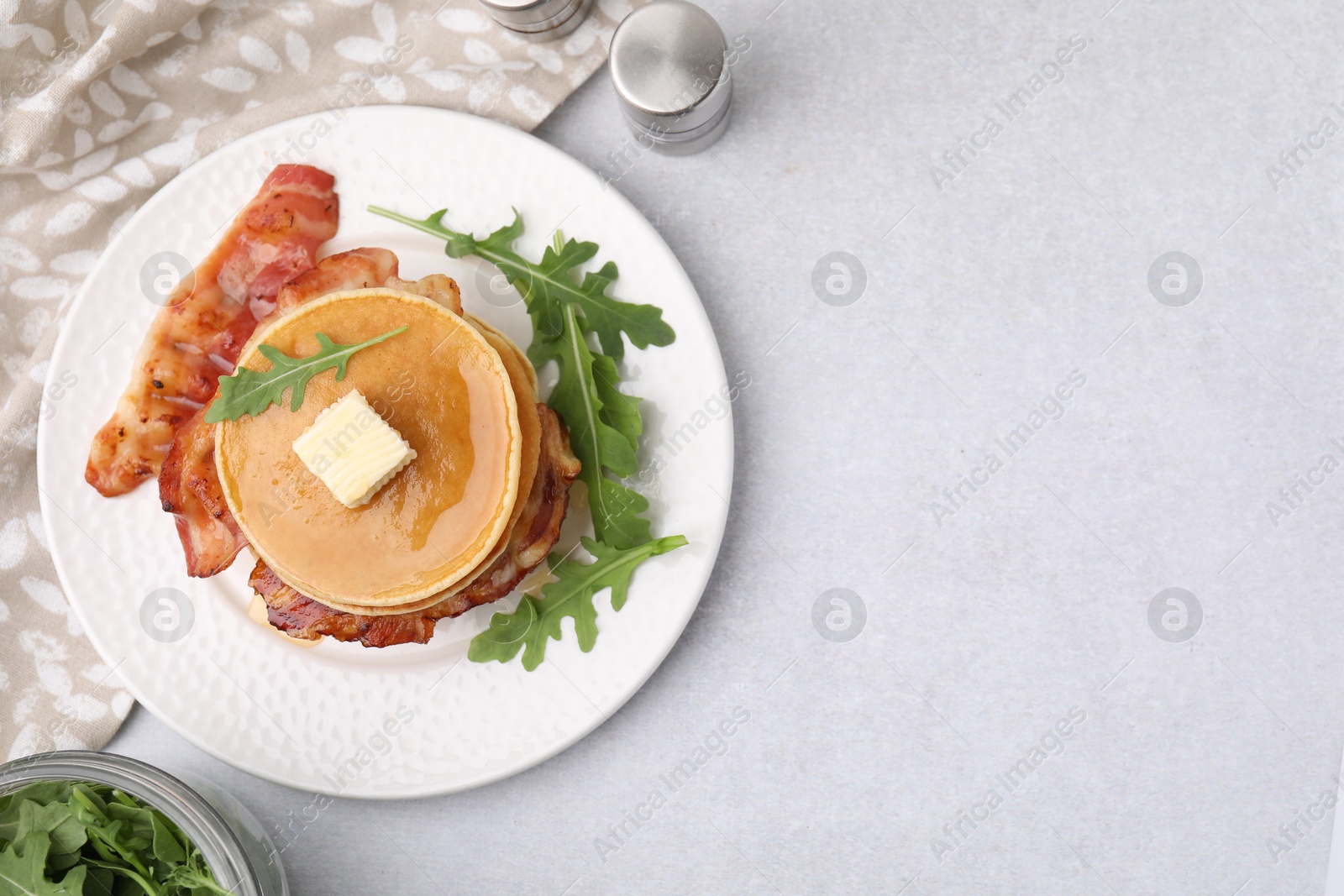 Photo of Delicious pancakes with bacon, butter and arugula on light table, flat lay. Space for text