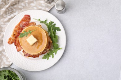 Delicious pancakes with bacon, butter and arugula on light table, flat lay. Space for text