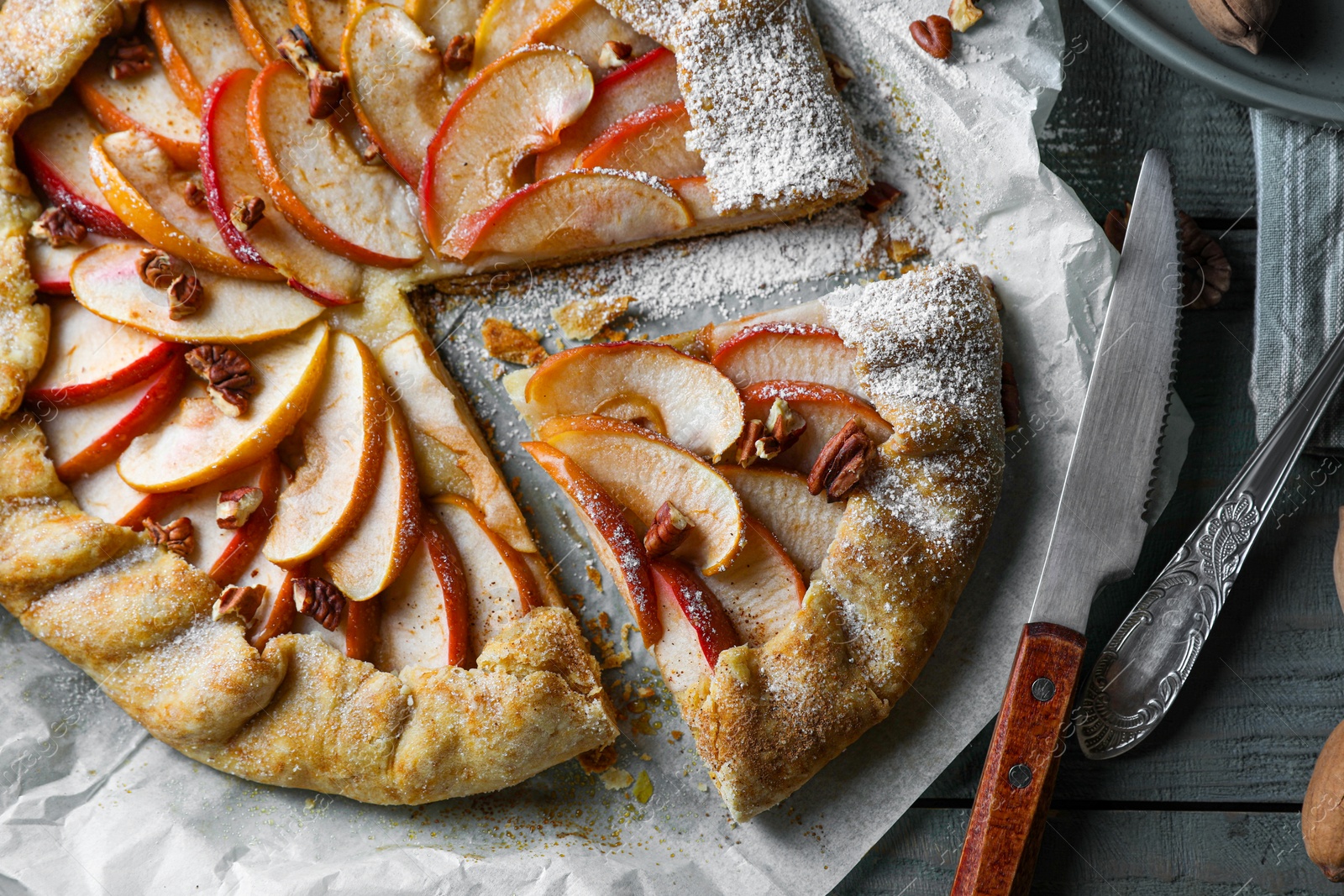Photo of Delicious apple galette with pecans and knife on wooden table, flat lay