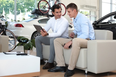Photo of Young salesman working with client in modern car dealership