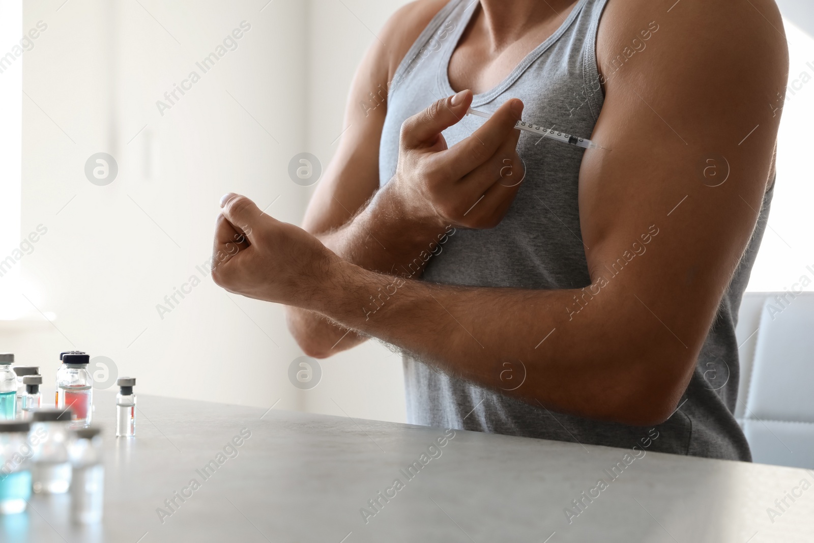 Photo of Athletic man injecting himself at table indoors, closeup. Doping concept