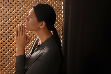Woman praying to God during confession in booth, space for text