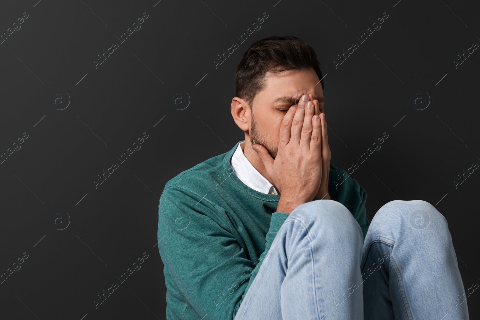 Photo of Upset man sitting on black background. Space for text