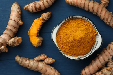 Photo of Bowl with turmeric powder and raw roots on blue wooden table, flat lay
