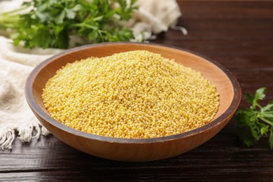 Photo of Millet groats in bowl and parsley on wooden table, closeup