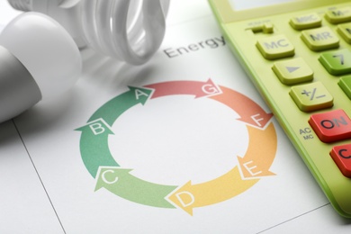 Photo of Energy efficiency rating chart, light bulbs and calculator on white background, closeup