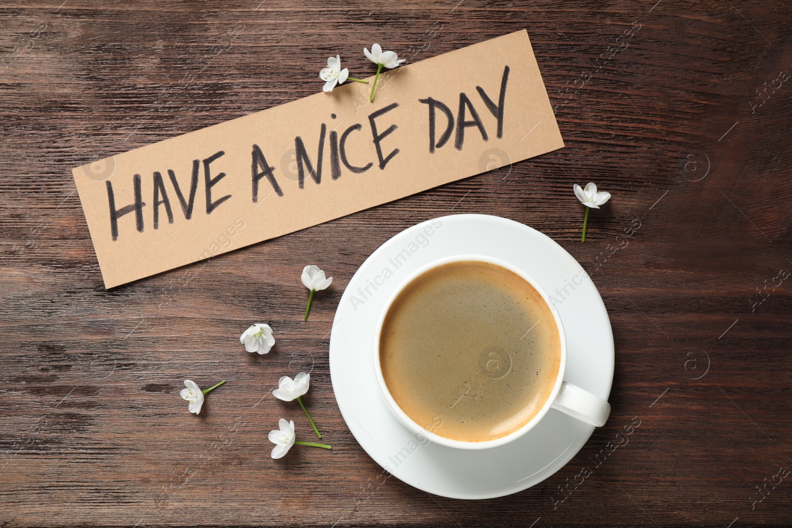 Photo of Delicious morning coffee, flowers and card with HAVE A NICE DAY wish on wooden table, flat lay