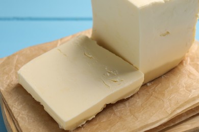 Photo of Block of tasty butter on light blue wooden table, closeup