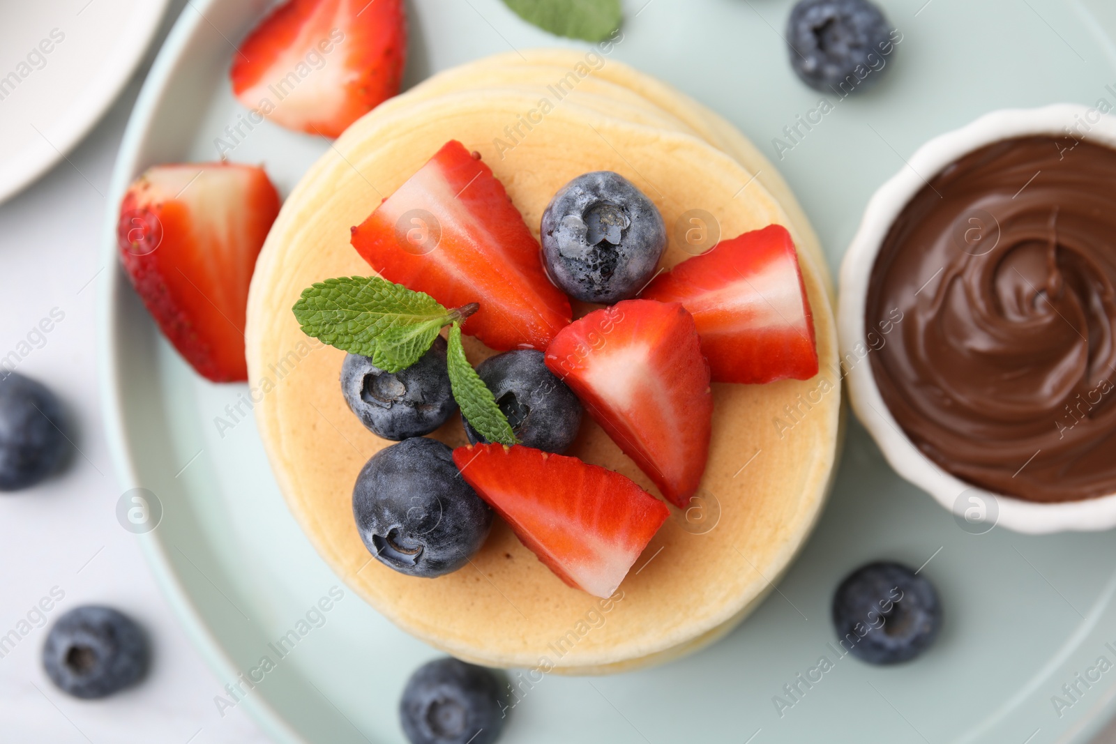 Photo of Delicious pancakes with strawberries, blueberries, mint and chocolate sauce on light table, top view