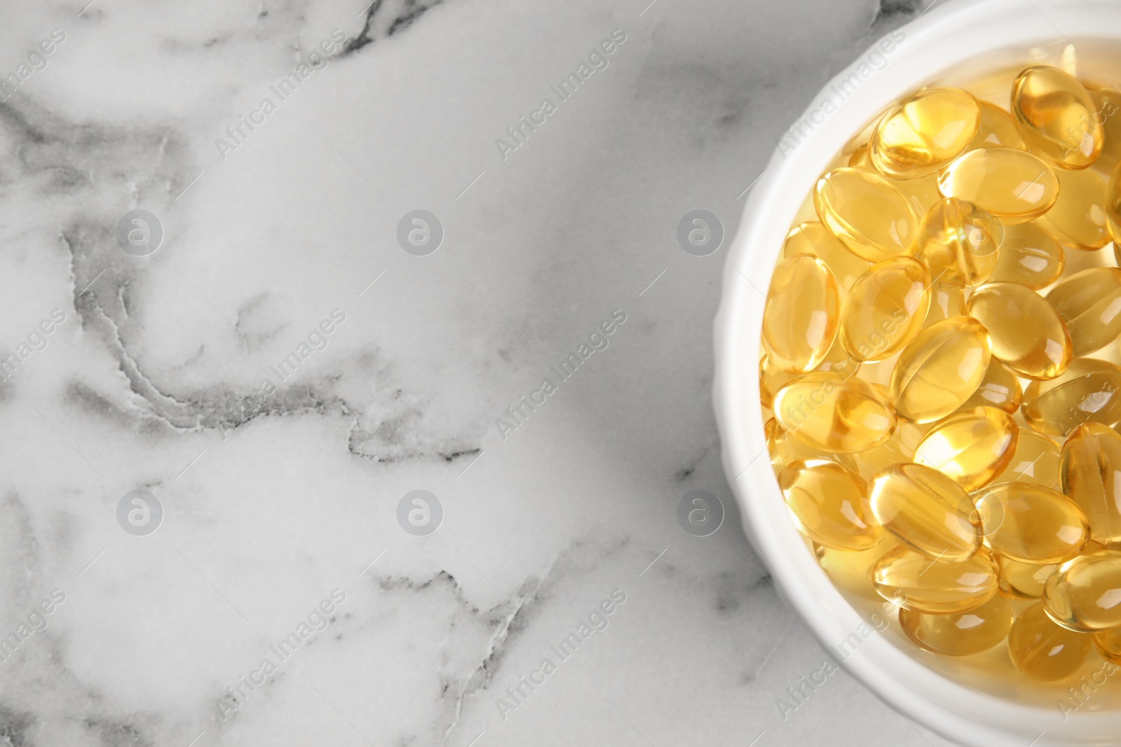 Photo of Bowl with cod liver oil pills and space for text on marble background, top view