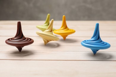 Photo of Bright spinning tops on light wooden table, closeup