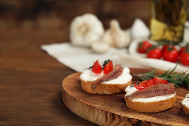 Delicious sandwiches with cream cheese, anchovies and tomatoes on wooden table, space for text