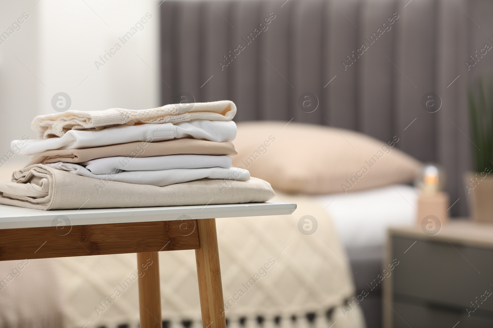 Photo of Stack of different folded clothes on bedside bench indoors, closeup. Space for text