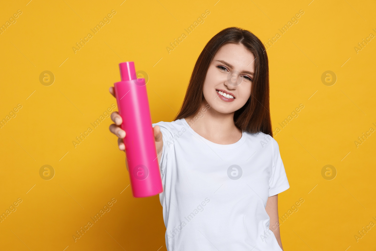 Photo of Beautiful young woman holding bottle of shampoo on yellow background