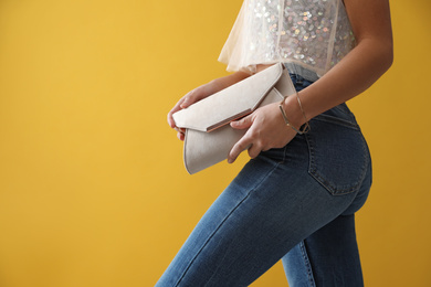 Woman in jeans with clutch purse on yellow background, closeup
