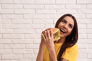 Photo of Young woman eating tasty burger near brick wall. Space for text