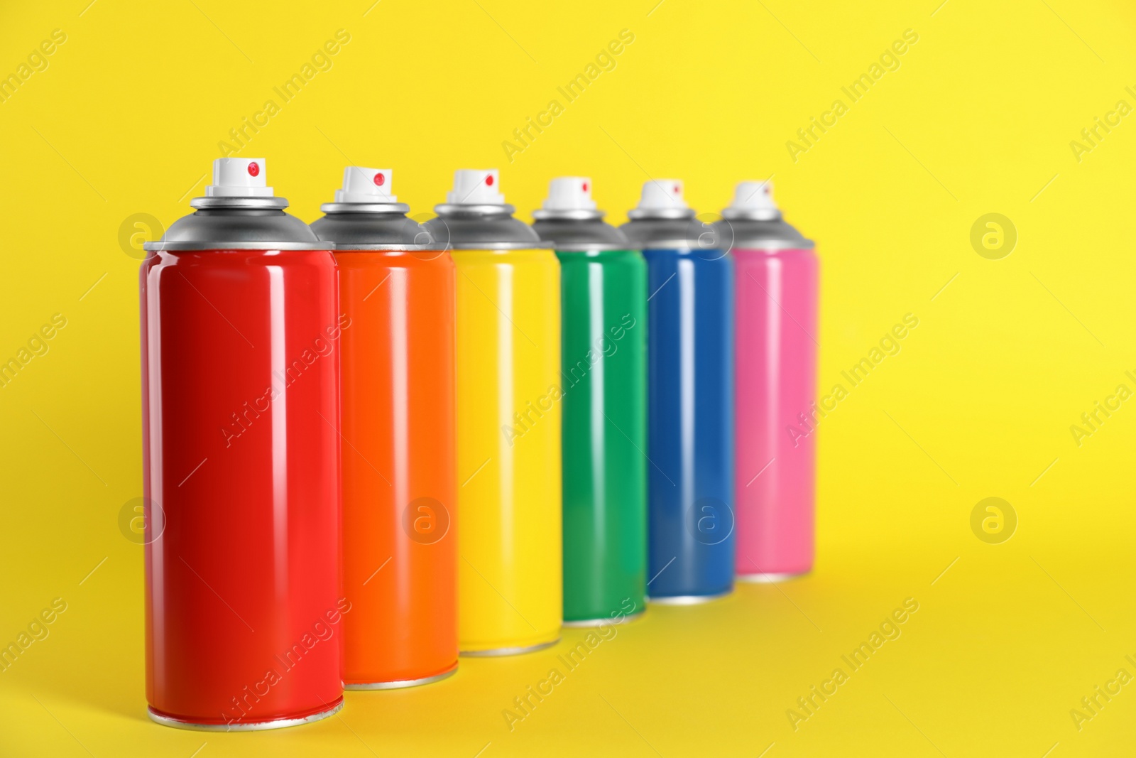 Photo of Colorful cans of spray paints on yellow background