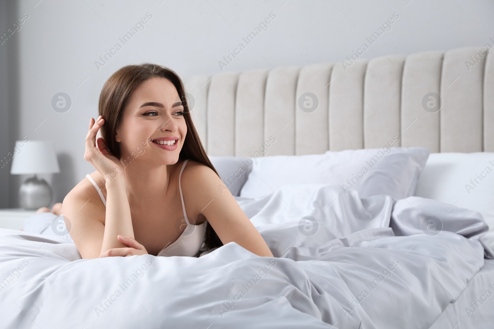 Photo of Young woman lying on comfortable bed with silky linens