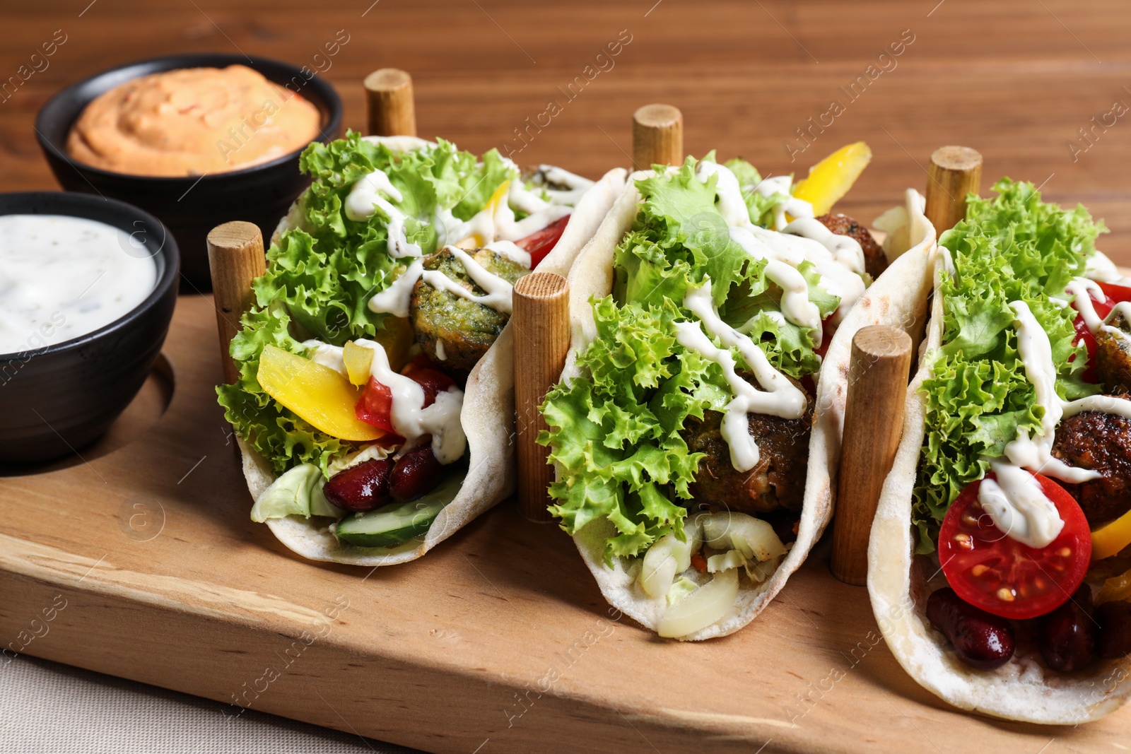 Photo of Delicious fresh vegan tacos served on wooden table, closeup