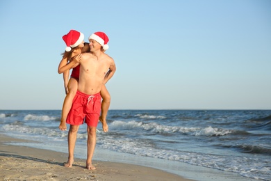 Happy couple with Santa hats together on beach. Christmas vacation