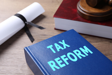 Image of Book with words TAX REFORM on wooden table, closeup