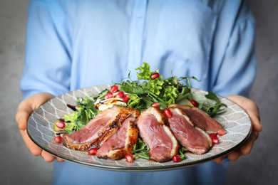 Photo of Woman holding plate with roasted duck breast on grey background, closeup