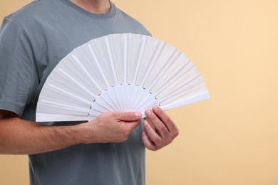 Photo of Man holding hand fan on beige background, closeup. Space for text