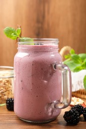 Photo of Delicious blackberry smoothie in mason jar and berries on wooden table