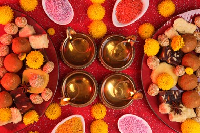 Photo of Diwali celebration. Flat lay composition with diya lamps and tasty Indian sweets on shiny red table