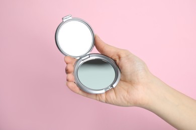 Woman holding stylish cosmetic pocket mirror on pink background, closeup