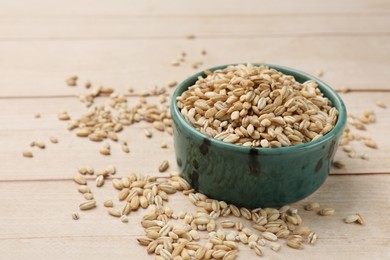 Photo of Dry pearl barley in bowl on light wooden table, closeup. Space for text