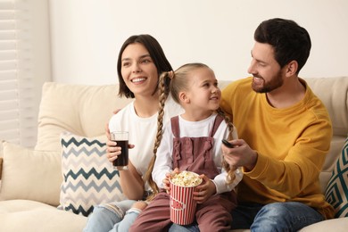 Happy family watching TV with popcorn on sofa indoors, space for text