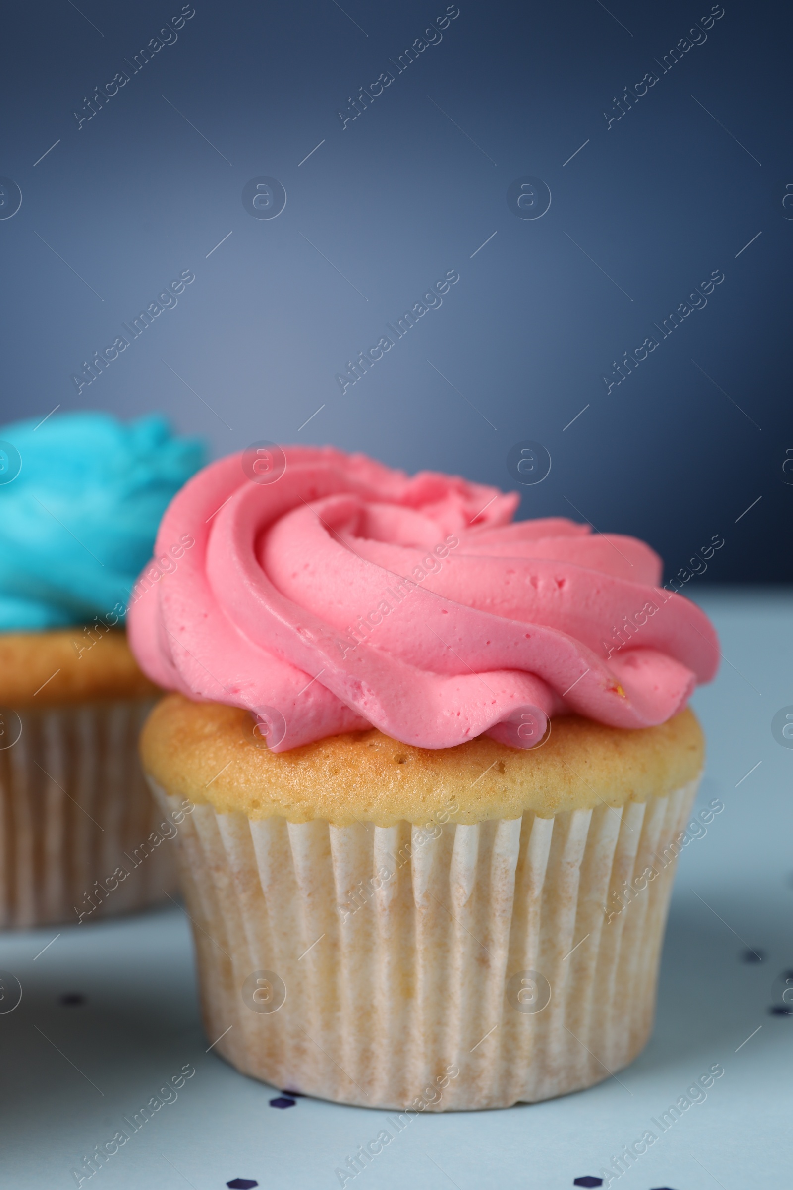 Photo of Delicious cupcakes with bright cream on blue background, closeup. Space for text