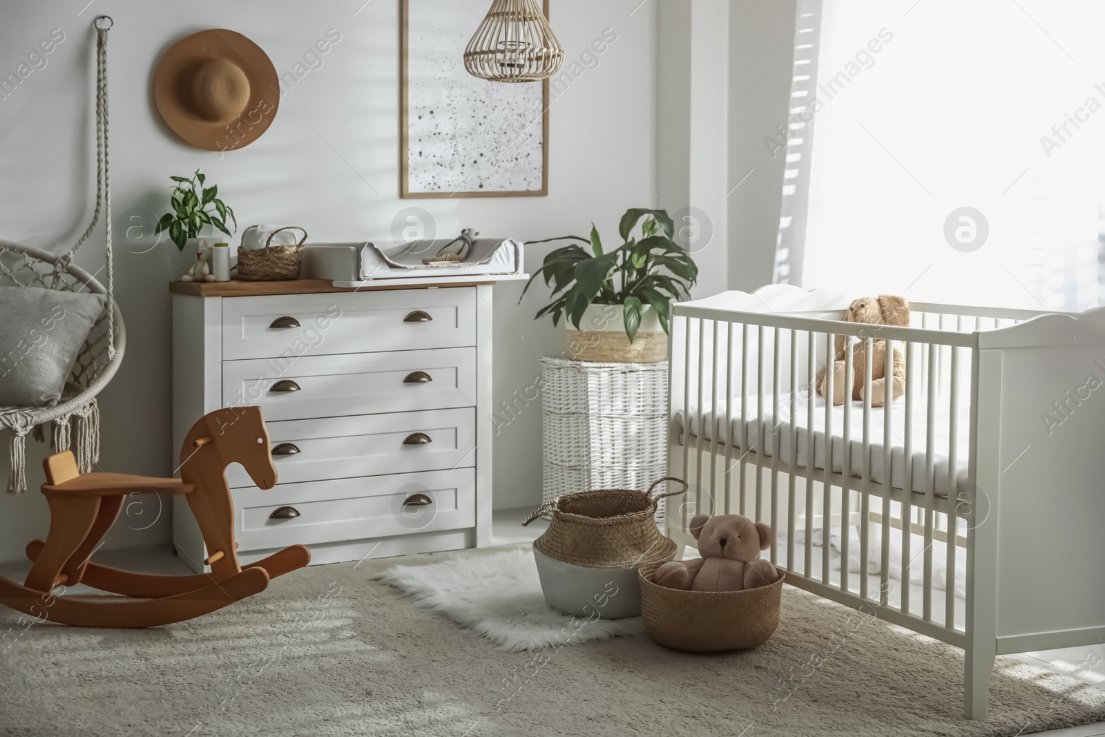 Photo of Chest of drawers with changing tray and pad near comfortable cradle in baby room. Interior design