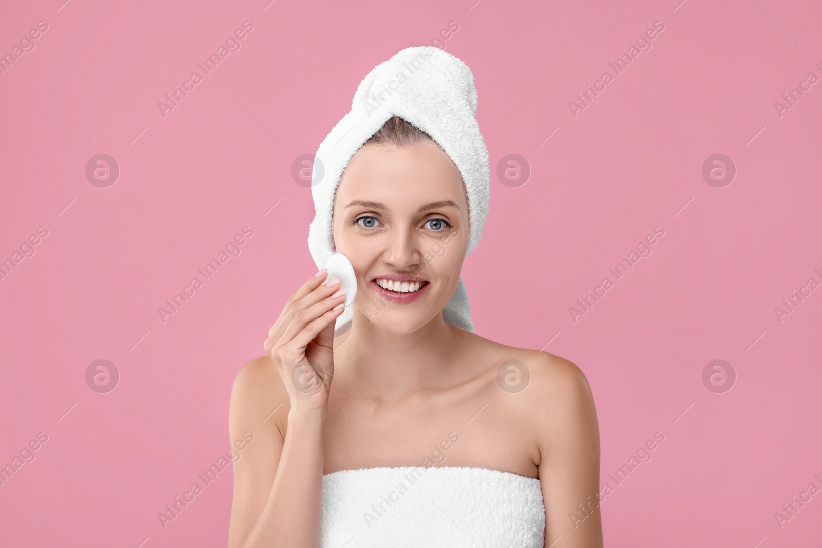 Photo of Young woman cleaning her face with cotton pad on pink background