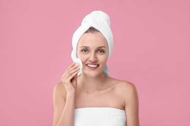 Photo of Young woman cleaning her face with cotton pad on pink background