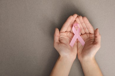 Photo of Woman holding pink ribbon on grey background, top view with space for text. Breast cancer awareness concept