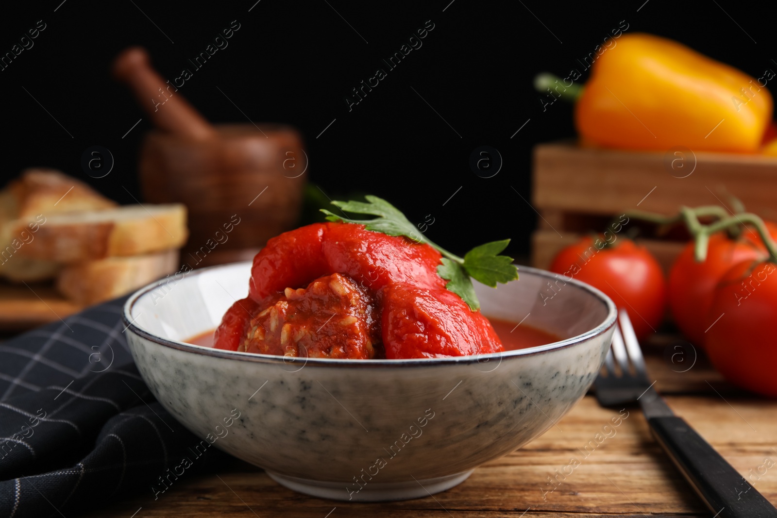 Photo of Delicious stuffed pepper with parsley in bowl on wooden table against dark background