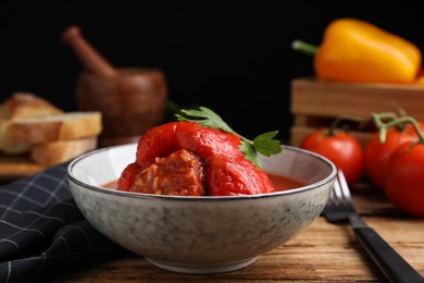Photo of Delicious stuffed pepper with parsley in bowl on wooden table against dark background